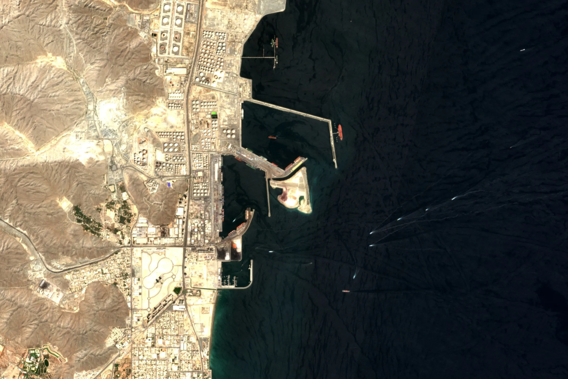 Satellite view of oil storage tanks and berths at Fujairah in the UAE, with ships at anchor offshore