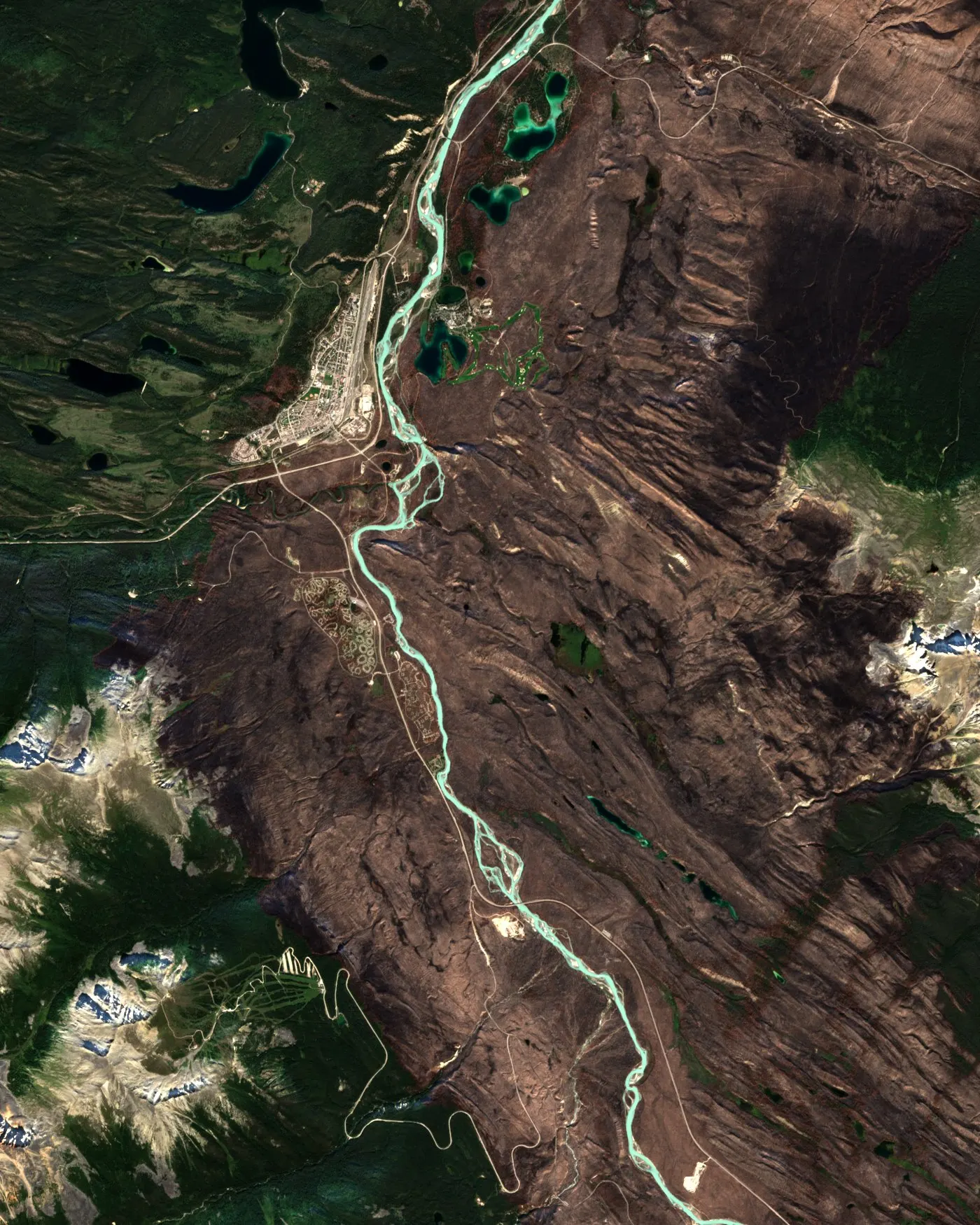 Satellite view of Jasper, Alberta, in September 2024, with the brown scar of the July wildfire filling the Athabasca valley to the edge of the town, the turquoise river running through it and unburnt green forest to the north-west