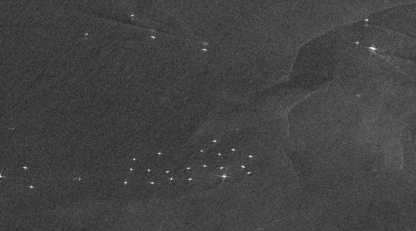 A dark grey radar image of open sea scattered with small bright white dots, many of them gathered in a loose cluster in the lower middle where ships wait at anchor.