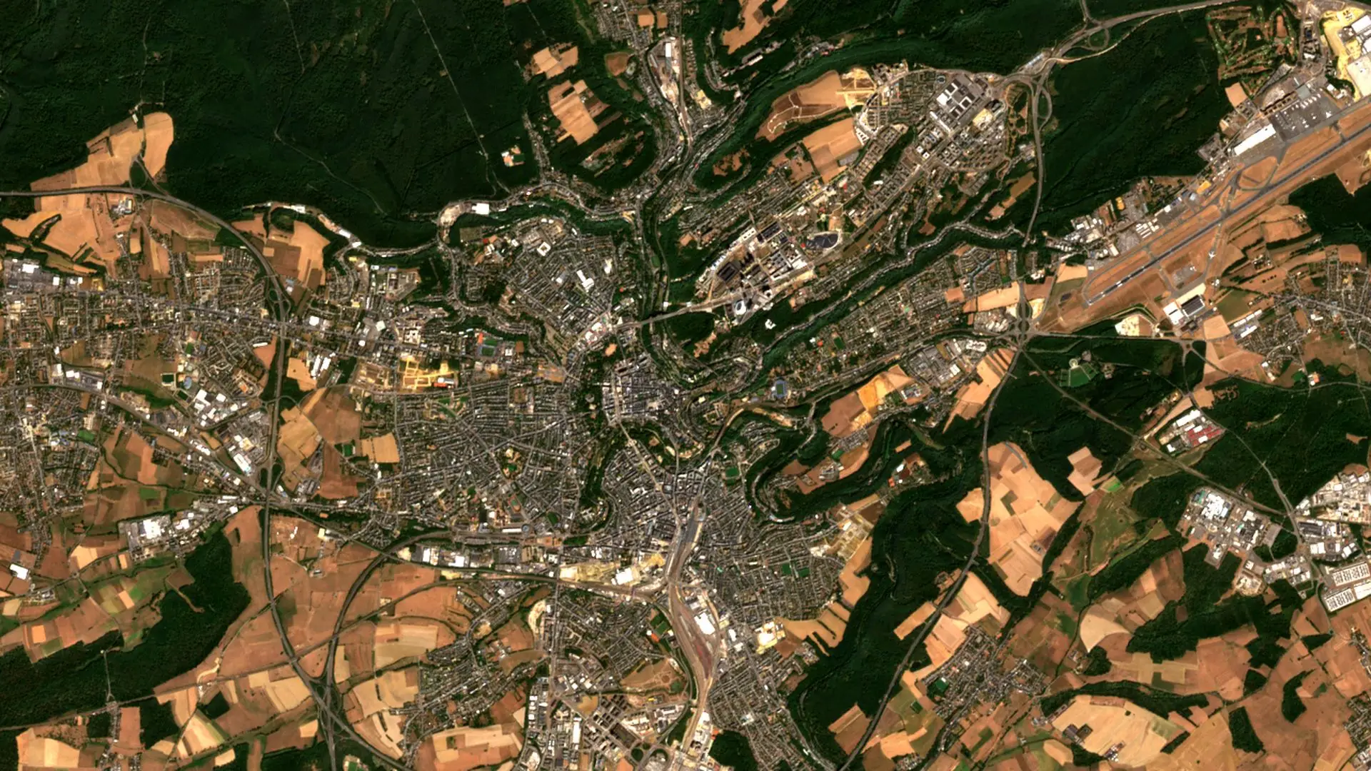 Sentinel-2 image of Luxembourg City, with wooded valleys winding through the city, the airport runway to the north-east and harvested fields all around. Luxembourg City, 14 August 2026