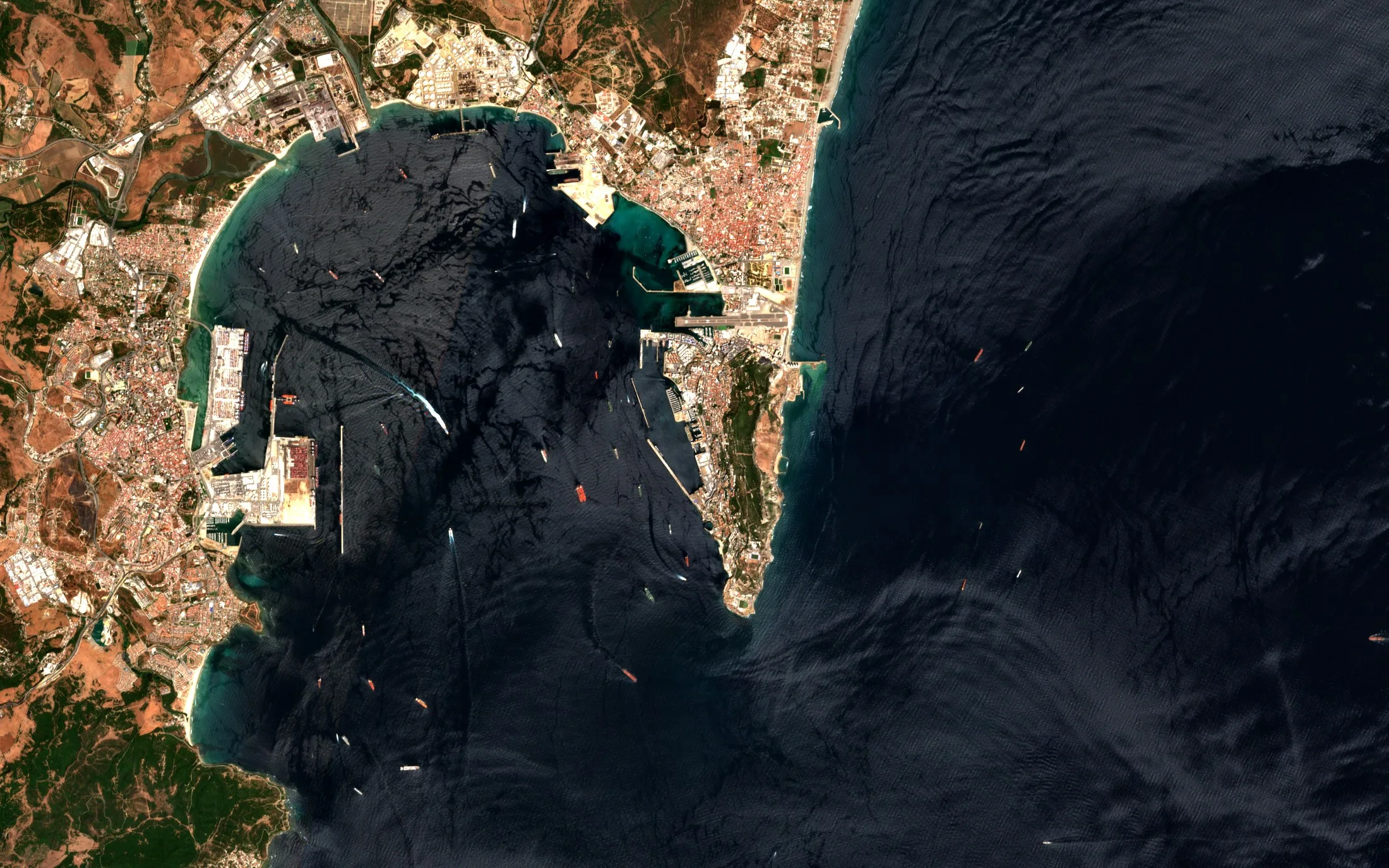 Satellite view of Gibraltar, with the Rock, the airfield across the isthmus, the harbour and ships at anchor in the bay and the strait